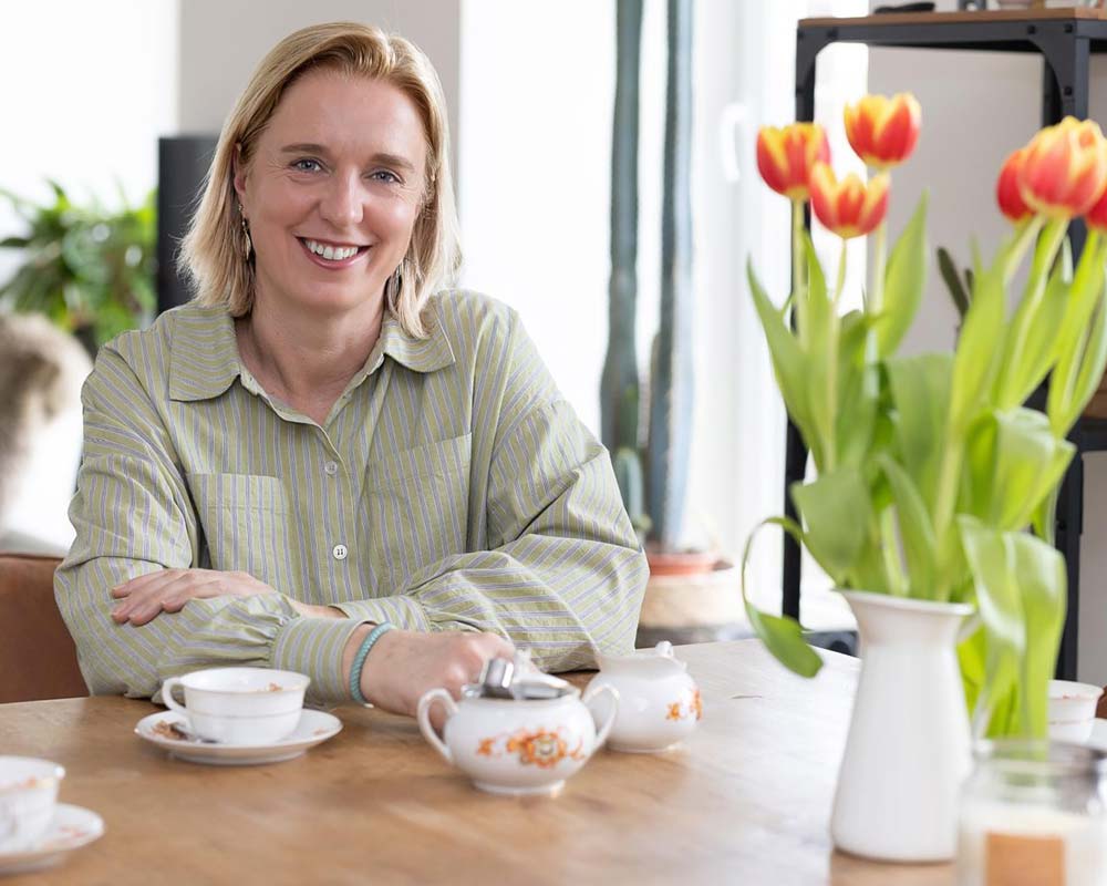 Katja Baumann, Bürgermeisterkandidatin in Uplengen, sitzt lächelnd an einem Tisch mit einer Tasse Tee